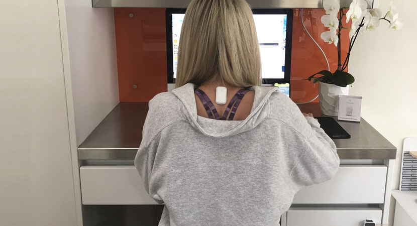 woman sits at a laptop with an Upright posture trainer between her shoulderblades